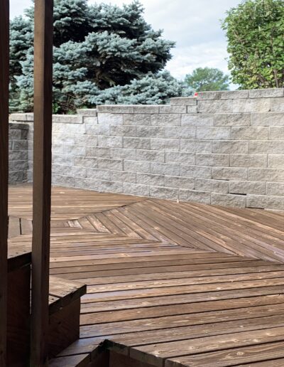 Large, wooden hexagon laid deck next to retaining wall.