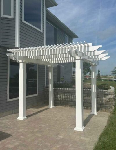 Sturdy, white, outdoor pergola in from of light grey house.