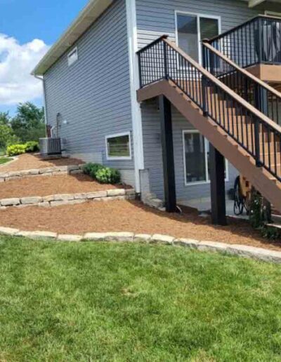 A beautiful new mulch beds created in a wavy shape on the side of a home with a beautiful new deck.